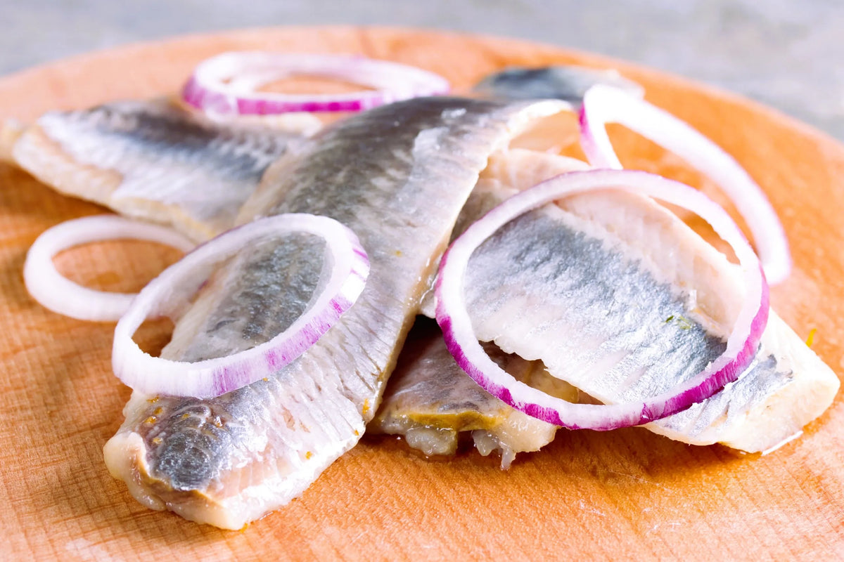 Sliced herring fillets with red onion rings on a wooden cutting board, a classic Swedish herring dish
