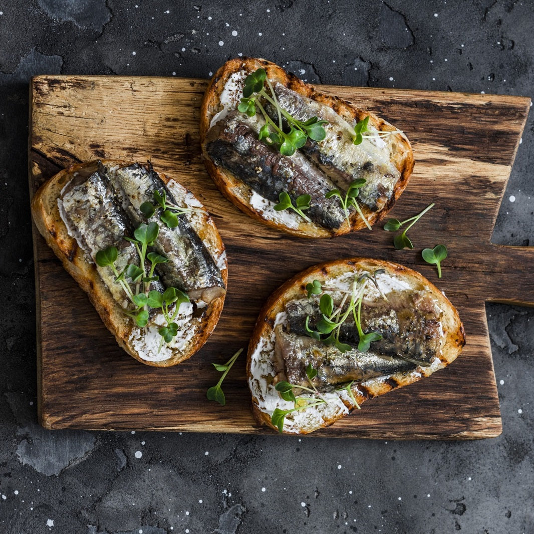 Tinned sardines on toasted bread with fresh microgreens on a wooden serving board